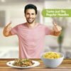 Smiling man in pink t-shirt giving double thumbs up with a plate of cooked noodles and a bowl of regular noodles on a wooden table, text overlay reads 'Tastes just like Regular Noodles'.